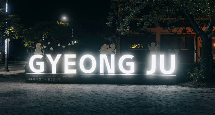 Letrero iluminado que dice GYEONG JU en un parque por la noche.