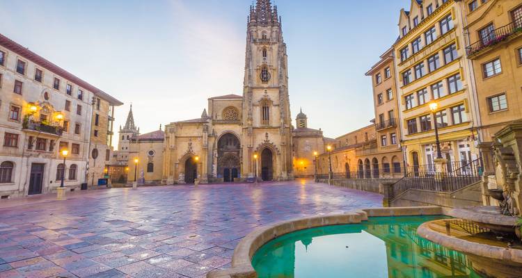 La lumière matinale baigne la cathédrale gothique d'Oviedo et la place tranquille avec une petite fontaine circulaire.