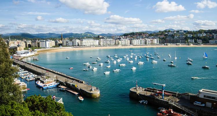 Vue panoramique de la baie de La Concha à Saint-Sébastien avec des bateaux à l'ancre, le front de mer et le paysage urbain environnant.