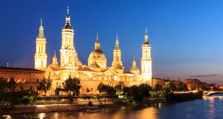 Basilique illuminée Notre-Dame du Pilier se reflétant sur l'Èbre au crépuscule à Saragosse.