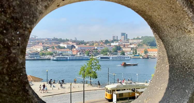 Quartier historique de Porto et fleuve Douro vus à travers une arche de pierre avec un tramway vintage qui passe.