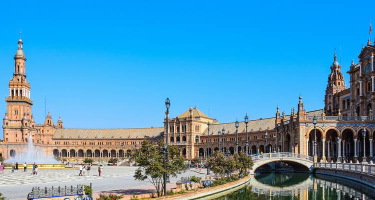 Weitläufige halbkreisförmige Plaza de España in Sevilla mit Türmen, Kanal und Springbrunnen unter klarem Himmel.