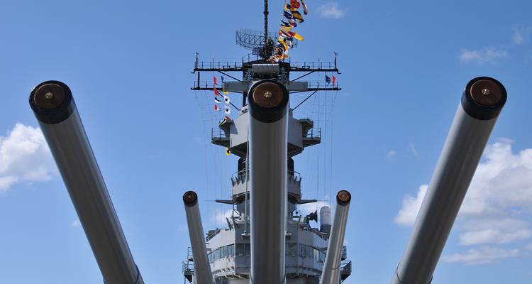 Vue de face des énormes canons d'un cuirassé et de sa superstructure décorée de pavillons de signalisation.