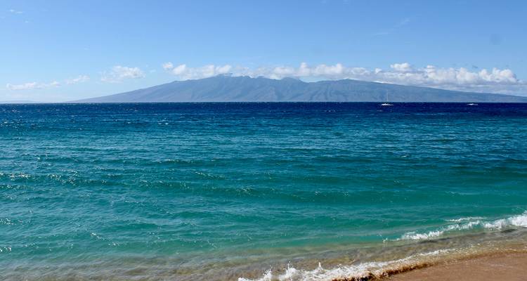 Eaux océaniques turquoise avec une île lointaine se dressant à l'horizon vue depuis une plage calme.