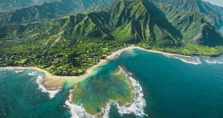 Vue aérienne de montagnes verdoyantes luxuriantes, de plages en croissant et de récifs coralliens vibrants le long de la côte de Kauai.