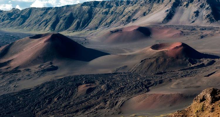 Cônes de scories volcaniques surnaturels et paysage de lave sombre à l'intérieur du cratère Haleakalā sous un ciel lumineux.