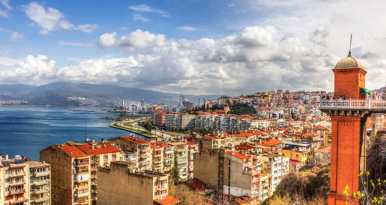 Panoramisch kustgezicht van Izmir met rode daken en een oude bakstenen lifttoren die uitkijkt over de baai.