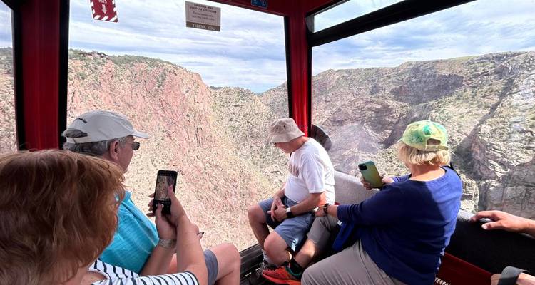 Turistas dentro de una góndola capturando fotos de un cañón rocoso y empinado muy abajo.