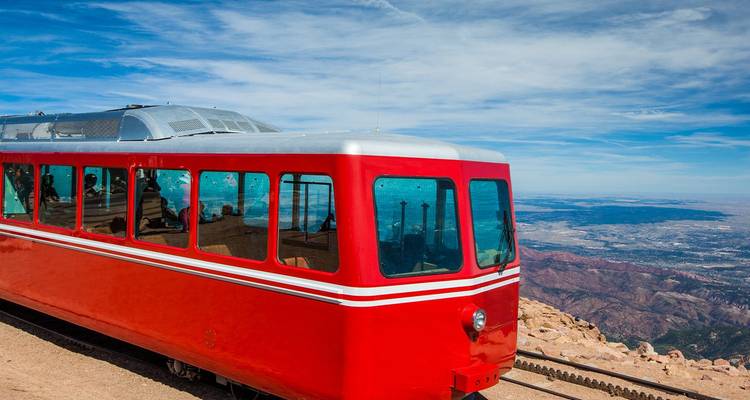 Vagón de ferrocarril de engranaje rojo brillante encaramado en la cima de una montaña con vistas expansivas del valle