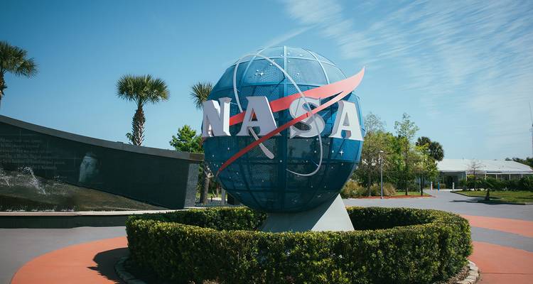 Große blaue NASA-Weltkugel im Kennedy Space Center, umgeben von Palmen unter einem hellen Himmel.