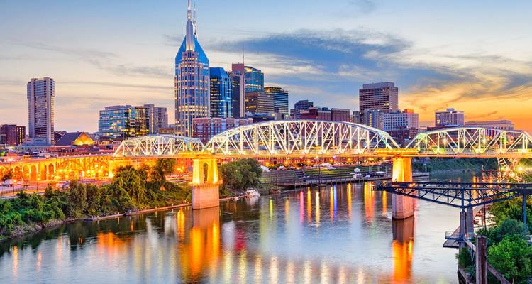 Vue du crépuscule de la ligne d'horizon de Nashville avec le pont illuminé se reflétant dans la rivière Cumberland sur un ciel coloré.