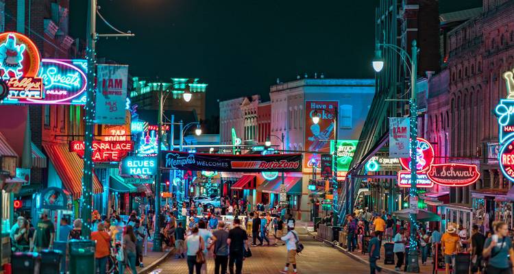 La rue Beale animée et illuminée par des néons, remplie de foules profitant de la vie nocturne de Memphis après le coucher du soleil.