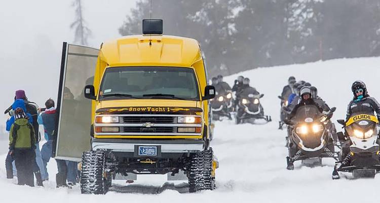 Autobús amarillo para nieve y conductores de motos de nieve embarcándose en un tour guiado de invierno a través del terreno nevado.