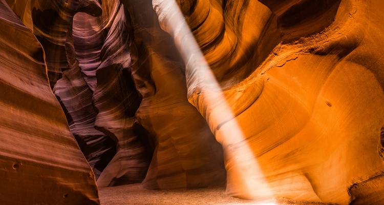 Rayon de soleil perçant les courbes de grès orange d'Antelope Canyon créant un jeu dramatique d'ombre et de lumière.