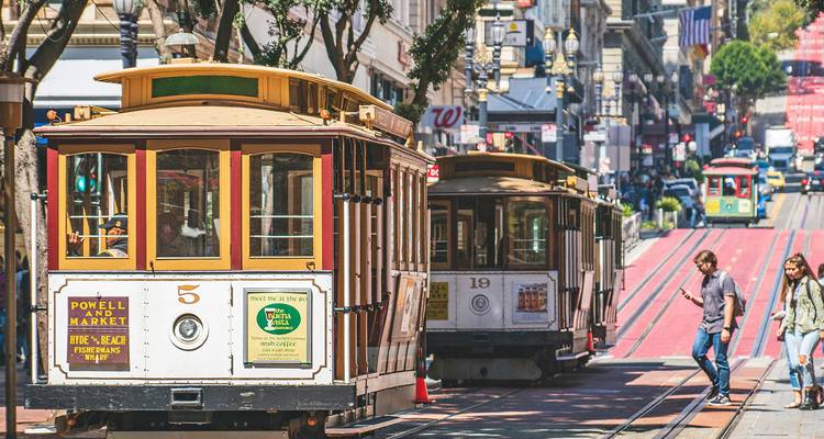 Historische San Francisco kabeltrams die een drukke stadsstraat oprijden die omzoomd is met winkels en voetgangers.
