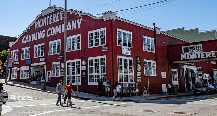Rood houten Monterey Cannery Row gebouw op een zonnige straat met bezoekers die voorbijlopen.