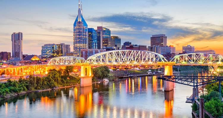 Vista nocturna colorida del horizonte de Nashville y el puente iluminado reflejándose en el río.