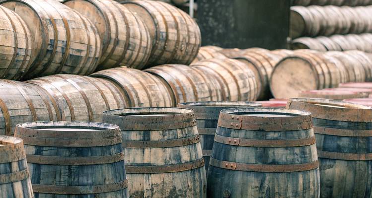 Stapels verweerde eiken whiskybarrels staan in rijen in een distilleerderijwarenhuis en roepen Schotlands whiskyerfgoed op.