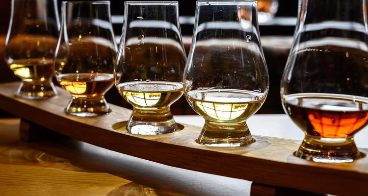 Rij met whiskyprobeerglasjes gevuld met gouden sterkedrank op een houten pallet in een distilleerderij