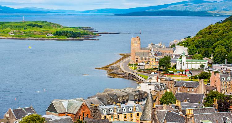 Ville côtière pittoresque d'Oban avec clocher d'église et îles au milieu des eaux bleues.