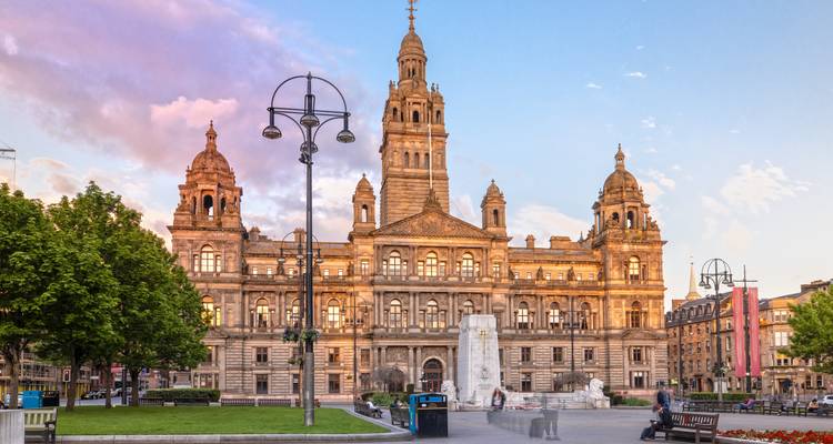 Grand bâtiment de l'hôtel de ville de Glasgow baigné dans la chaude lumière du coucher de soleil avec des piétons flous sur la place.