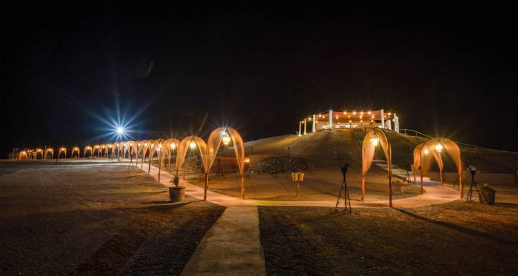 Restaurante iluminado en la cima del desierto con pasarela arqueada iluminada que conduce hacia arriba en la oscuridad.