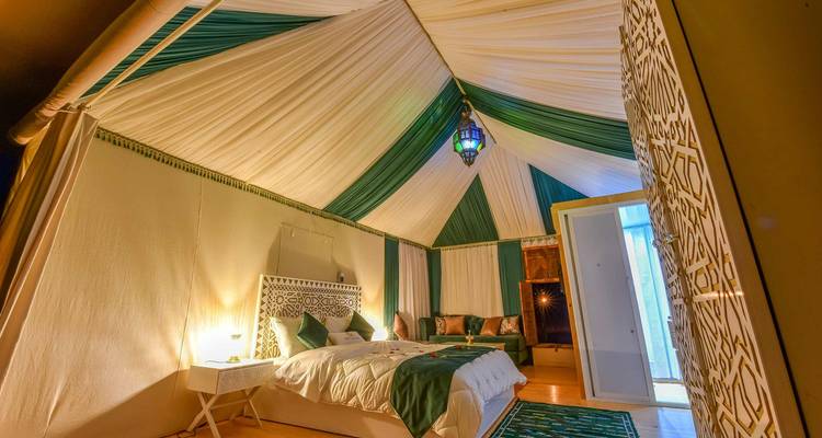 Amplia tienda de lona con techo drapeado verde y blanco, cama elegante e iluminación de farol marroquí.