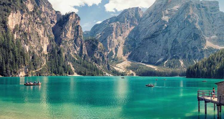 Lago alpino turquesa rodeado de bosques de pinos con imponentes picos rocosos en los Dolomitas.