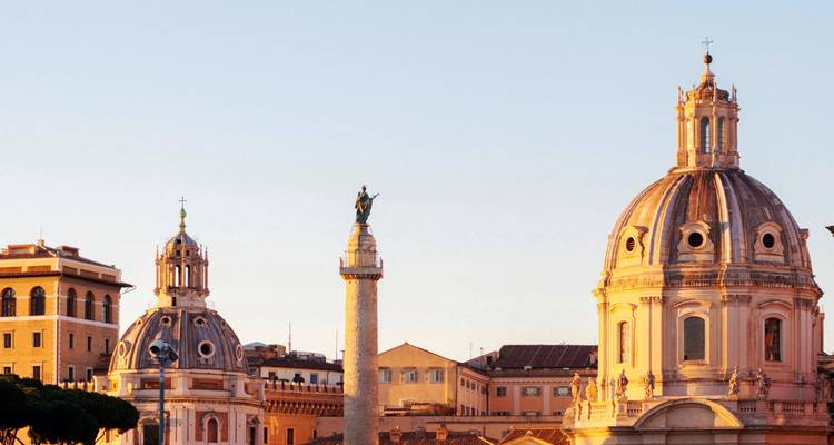 Cálida luz del atardecer sobre la Columna de Trajano de Roma y las cúpulas gemelas de iglesias barrocas.