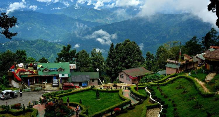 Vue surélevée sur des terrasses verdoyantes luxuriantes, des toits et des montagnes brumeuses au loin sous un ciel partiellement nuageux.