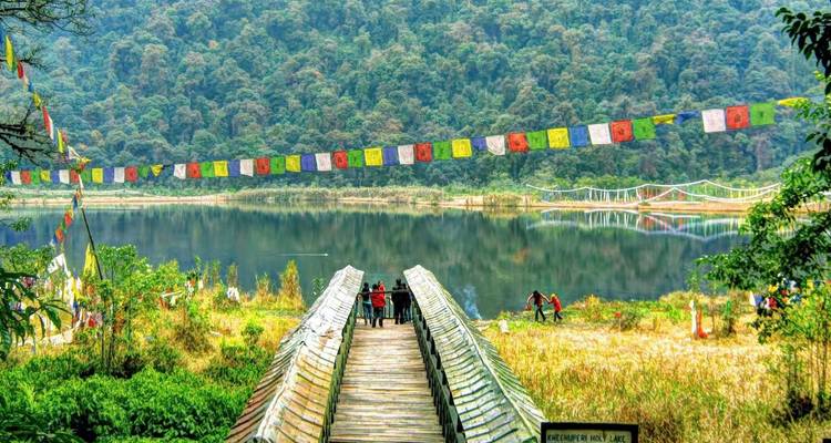 Lac serein bordé par une forêt dense avec une guirlande de drapeaux de prière multicolores traversant l'eau.
