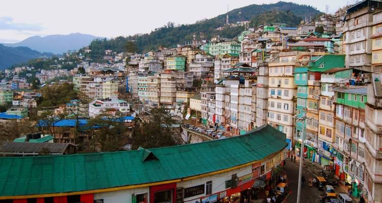 Vue panoramique d'une ville étalée sur les collines avec des bâtiments aux couleurs pastel et des rues sinueuses.