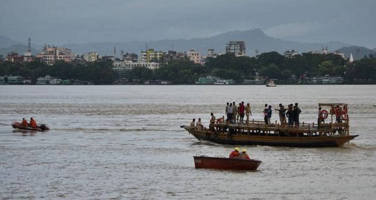 Boats and ferry cross a wide river with distant city skyline and hills