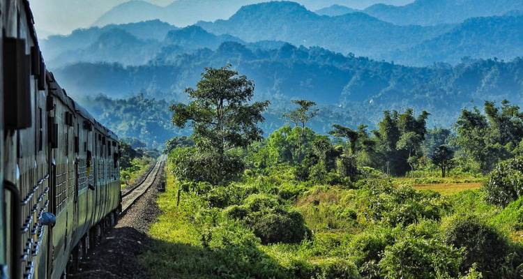 Passenger train curving through lush green valley with layered blue hills beyond