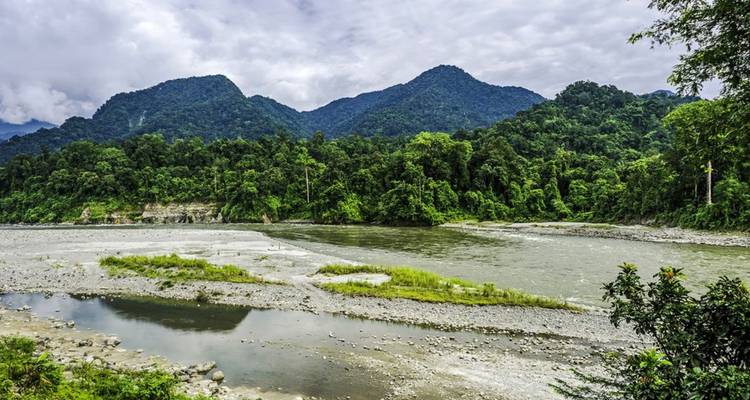 Clear river bends through dense rainforest with tall green mountains under cloudy sky
