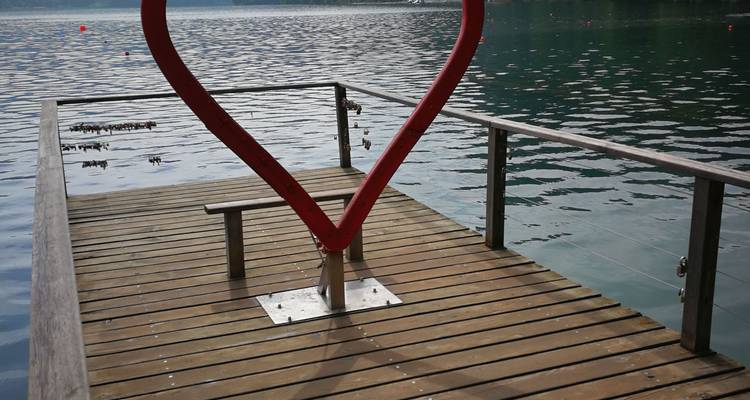 Jetée en bois avec sculpture de cœur rouge et cadenas d'amour au-dessus d'un lac calme