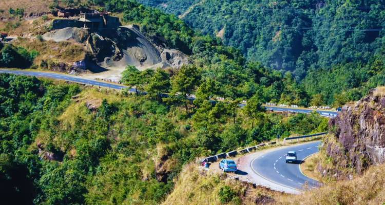 A winding mountain road cutting through lush green hills with vehicles making the ascent.