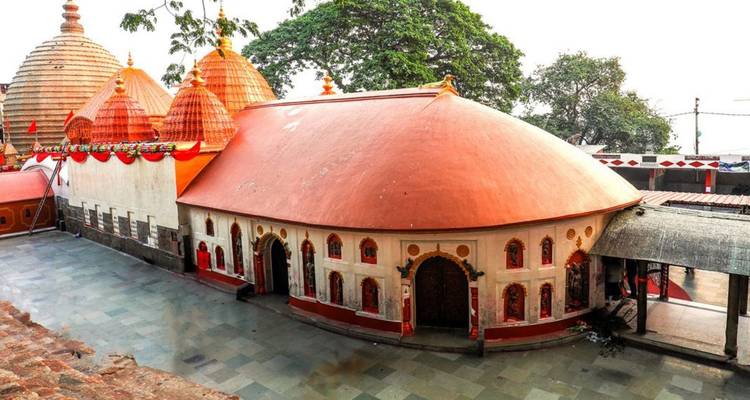 The terracotta domes of Kamakhya Temple stand out against white walls and greenery.
