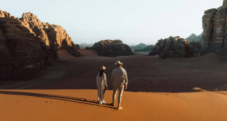 Couple se tenant la main en marchant à travers le vaste sable orange entouré par les formations rocheuses spectaculaires du Wadi Rum.