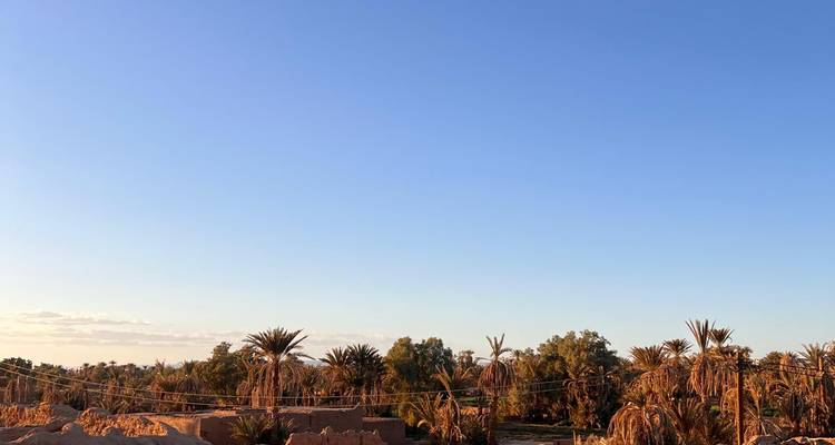 Klarer blauer Himmel über einer kargen Wüstenoase mit Palmen und Lehmgebäuden