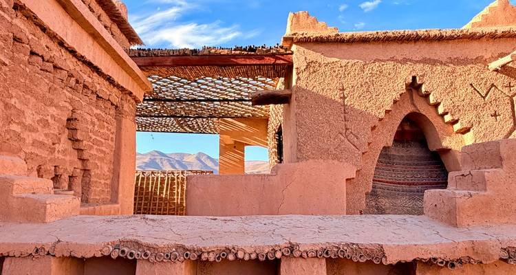 Murs et arches de kasbah en adobe chaleureusement éclairés avec des ombres à motifs projetées par un toit en treillis de bois.