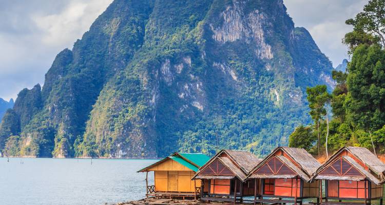 Rustikale schwimmende Bungalows ruhen auf einem smaragdgrünen See unter hoch aufragenden Kalksteinbergen im Khao Sok Nationalpark.