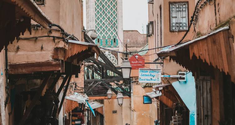 Ruelle étroite de médina avec des auvents en bois et un minaret aux tuiles vertes qui s'élève en arrière-plan