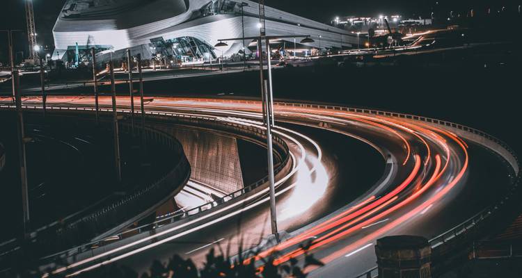 Prise de vue nocturne en pose longue d'une autoroute courbe avec des traînées lumineuses près d'un bâtiment moderne
