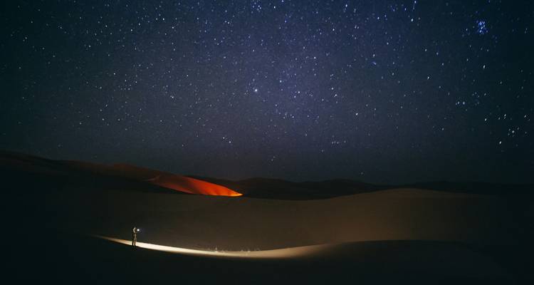 Ciel étoilé au-dessus des dunes sombres du Sahara avec une silhouette solitaire tenant une lanterne