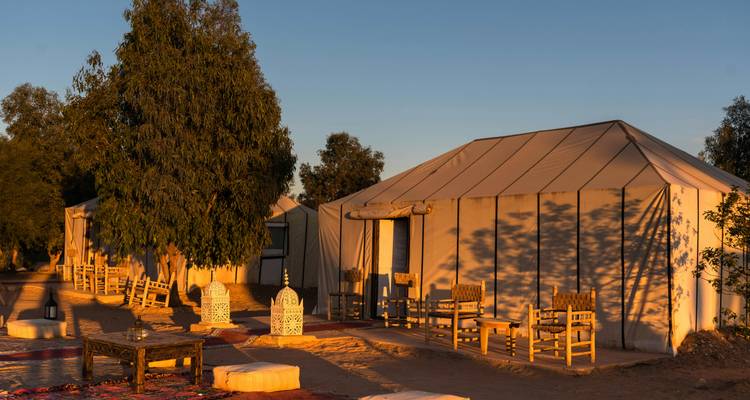 Site de glamping dans le désert avec tentes en toile et mobilier en bois baignés dans une lumière chaude du soir