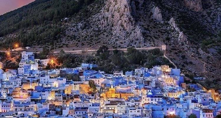 Panorama au crépuscule des maisons bleues de Chefchaouen regroupées sur une pente avec des montagnes rocheuses en arrière-plan