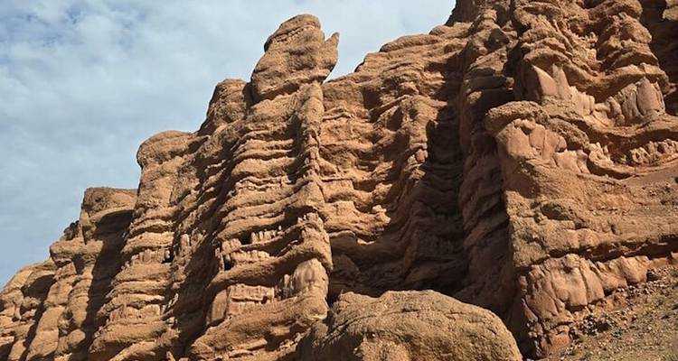 Las formaciones de roca roja en capas se elevan bajo un cielo marroquí parcialmente nublado.