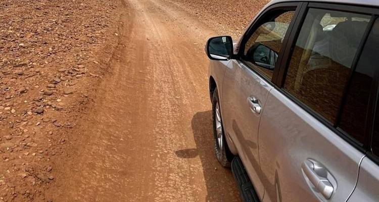 Vehículo plateado 4x4 conduciendo por un áspero camino desértico rojizo rodeado de terreno rocoso.
