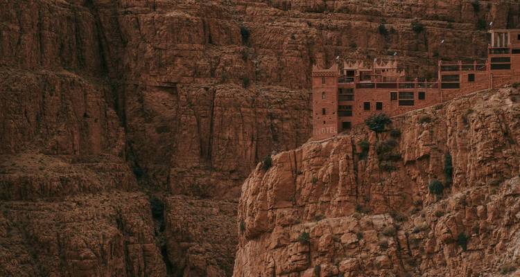 Un complejo hotelero de piedra rojiza construido en los acantilados de un cañón imponente dentro de una garganta desértica.